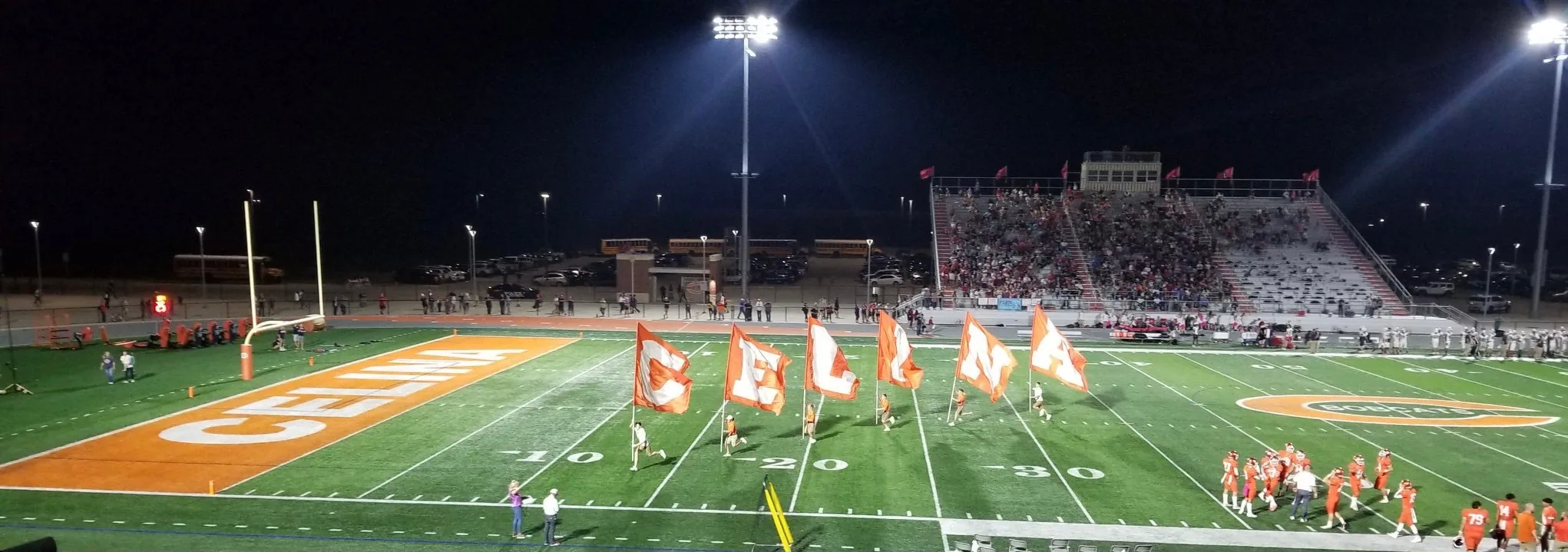 Flag runners lead a team onto the field under the lights at a Friday night high school football game at Celina High School in Texas.