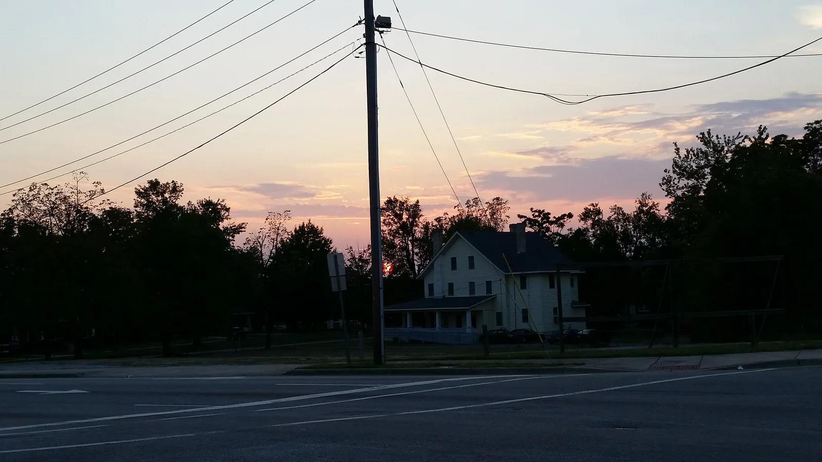 The sun sets over a house and a street corner in High Point.